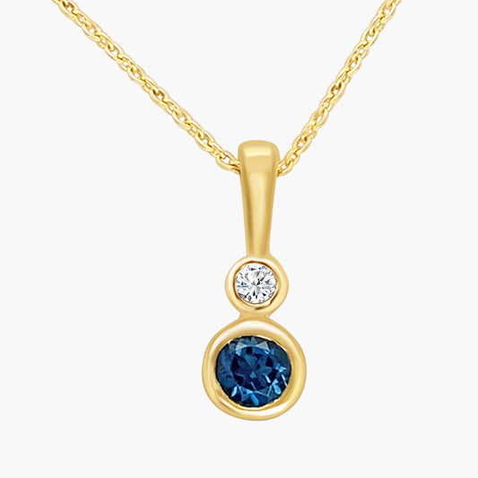 Gold pendant with blue gemstone and clear stone on a white background